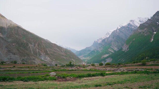Wide angle shot of farms in front of snowy Himalayan mountain peaks during the summer season as seen near Muling village in Lahaul and Spiti district, Himachal Pradesh, India. Natural background.