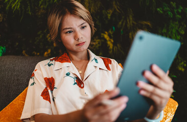 Focused Asian woman holding tablet and stylus, expressing curiosity and analysis, symbolizing digital learning and freelance adaptability through technology. © BullRun