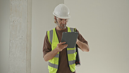 Man architect in hardhat and vest holding tablet and checking plans inside building  planning concentration. © Krakenimages.com