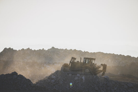 Aerial view of a heavy bulldozer moving rocks in an open-pit mine with dust rising in the air Santa Lucia de Gordon, Castile and Leon, Spain.