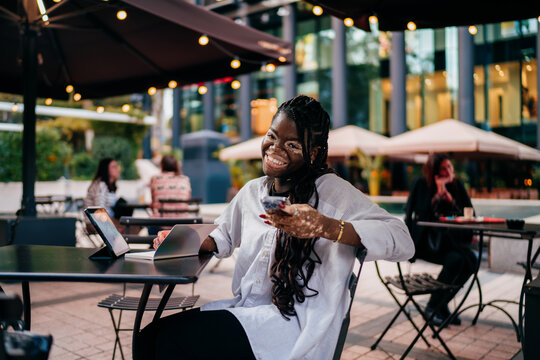 Happy woman with vitiligo skin condition using mobile banking app on smartphone in outdoor cafe, successful freelancer checking account balance near digital tablet, financial freedom concept