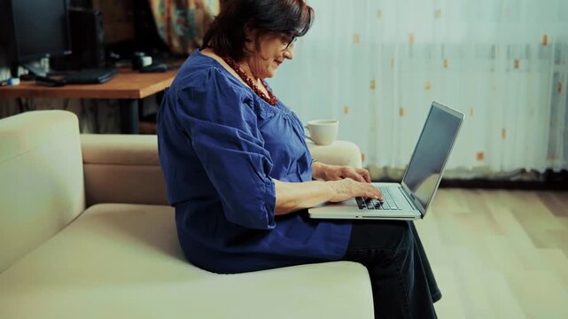 Senior Person Typing On Laptop While Sitting On Sofa At Home. Digital Literacy For Seniors. Using Notebook For Education