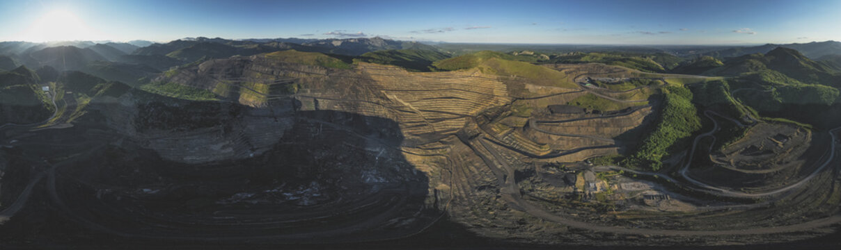 Aerial view of the massive open-pit mine terraces and winding industrial roads surrounded by green mountains in Santa Lucia de Gordon, Castile and Leon, Spain.