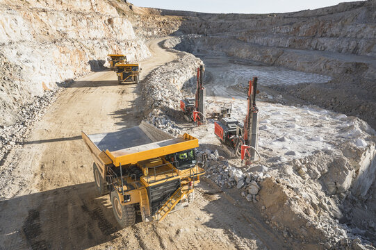 Aerial view of an open-pit mine featuring large yellow dump trucks and drilling rigs on rocky terraces in Santa Lucia de Gordon, Castile and Leon, Spain.