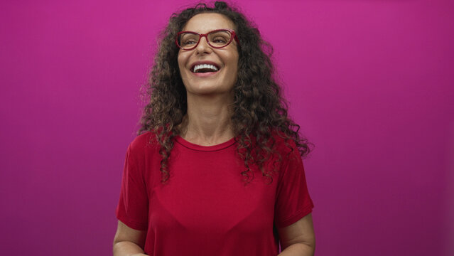 Hispanic woman wearing red shirt wipes tears from cheeks in studio; sadness sorrow grief vulnerability.