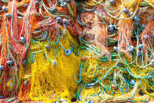 Full frame background of colorful tangled fishing nets with yellow, orange, and blue ropes and floats used in traditional commercial fishing industry.