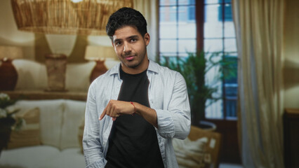 Naklejka premium Smiling man pointing index finger down with right hand toward floor in studio living room set; playful confidence.