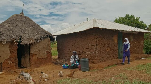A young girl uses water near a mud house while a woman does chores in a rural African village. The scene highlights daily life, limited water resources, and the importance of water in basic routines.