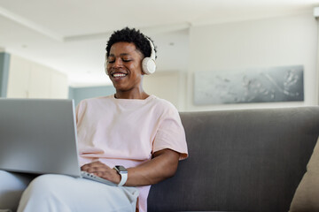 Vertical video: Smiling man in pink tee working on laptop at home, with white headset, smartwatch © wavebreak3