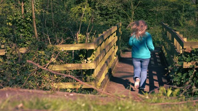 Woman running across wooden bridge woodland in dappled summer sunshine