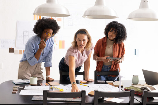 Vertical video: Diverse female colleagues pointing at blueprints after client feedback at studio