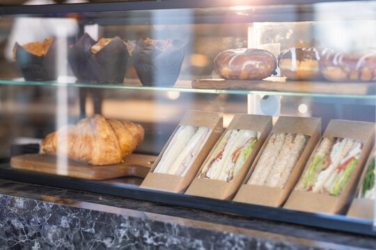 Four packaged triangular sandwiches are sitting inside glass display on marble counter, warm light