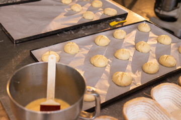 Two parchment-lined trays holding scored rolls are proofing on stainless counter with pastry brush © wavebreak3