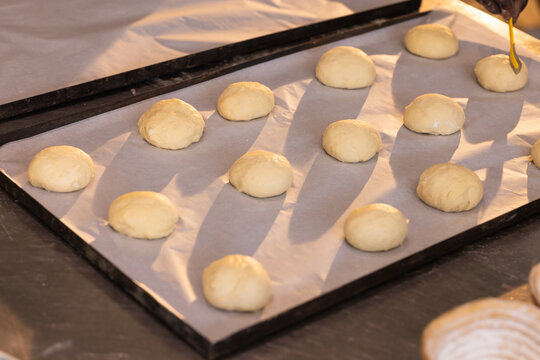 Parchment pan holding raw rolls at bakery counter with yellow brush and floured proofing basket