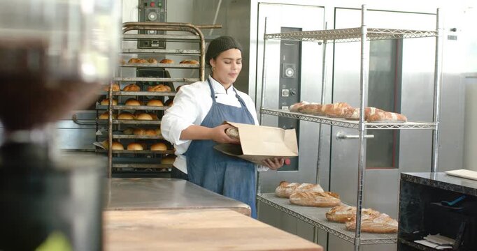 Order African American woman baker in chef jacket taking loaf into bag folding, walking to POS