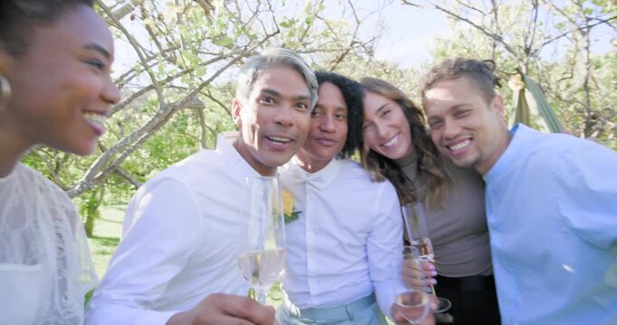 Diverse friends one raising flute sparking wedding toast showing ring to camera outside under drape