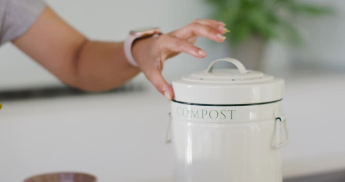 Hands lifting compost lid after peeling fruit and placing peels into countertop can for composting