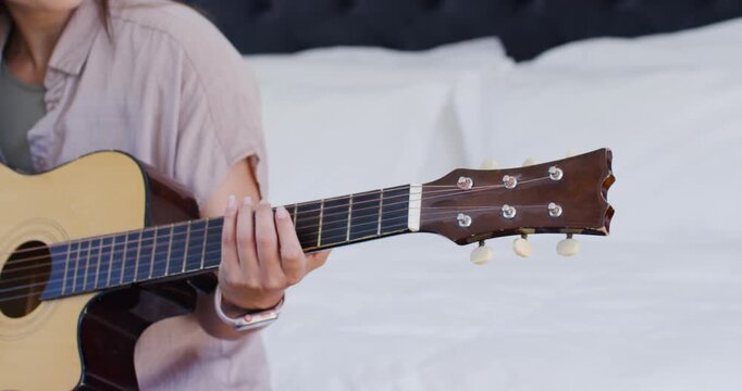African American woman starting fingering chords near headstock, practicing acoustic guitar on bed
