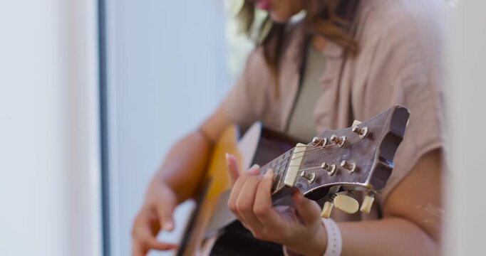 African woman placing left hand, camera pulling back, playing guitar singing along by window watch