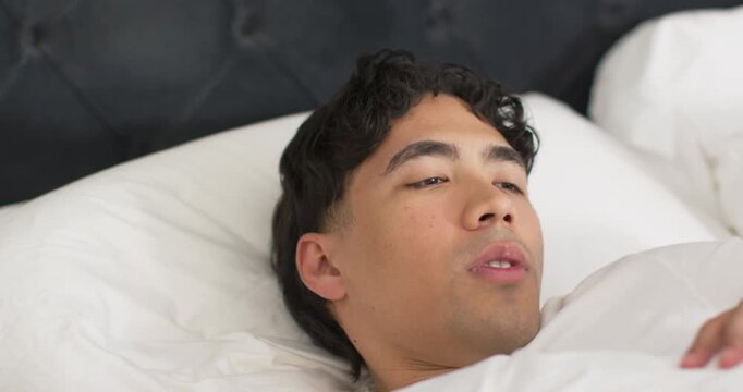 Morning light rousing man lying on bed, stirring, sitting up, rubbing chest and stretching