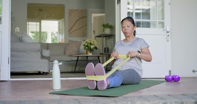 Senior Asian woman in sportswear picking up band, looping shoes, pulling for strength on porch mat
