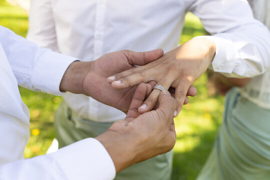 Three African American adults in white shirts placing multi-band ring on left ring finger in garden