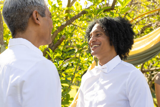 Two men celebrating at ceremony start in garden with draped fabric, white shirts, sunlight on faces