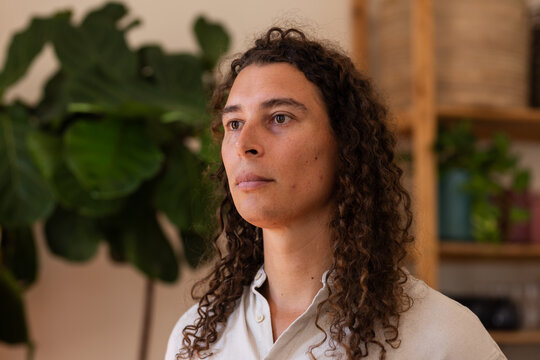 African American non-binary person posing at home wearing beige collared shirt by shelf and plants