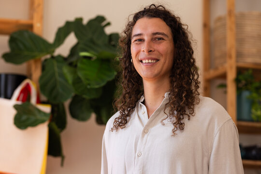Adult nonbinary African American standing, smiling in warm studio with fig plant and beige shirt