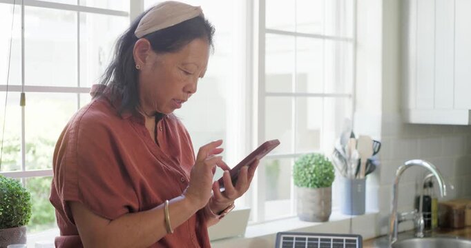 Senior Asian woman sitting kitchen counter after tapping phone plugging cables to solar panel