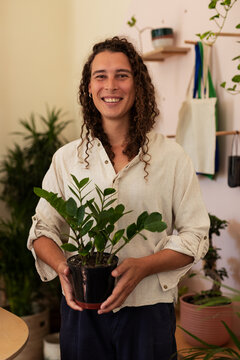 African American nonbinary wearing linen shirt holding ZZ plant in shop, smiling with black pot