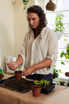 Non-binary African person repotting seedlings at home bench with seedling tray, wearing linen shirt