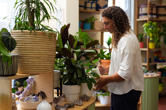 Non-binary African American person tending plants at boutique with watering vessel, copy space