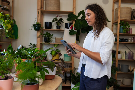 Non-binary person wearing white shirt, holding tablet, arranging pots on wooden table, copy space
