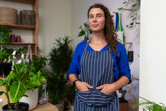 African American nonbinary adult in striped apron tending plants on wooden table in plant shop