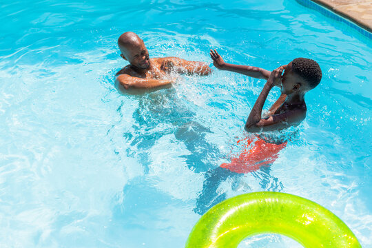 African American males, adult splashing, youth shielding nose, playing in pool with neon green ring