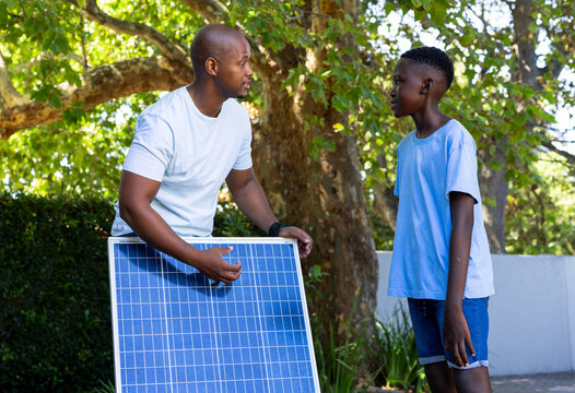 Adult male holding blue solar panel while youth male learning during solar setup in garden