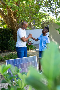 African man and teenage boy clasping hands after smartphone showing solar panel reading in garden