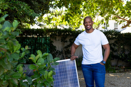 Man leaning on freestanding solar panel in residential backyard, smiling, wearing wristwatch