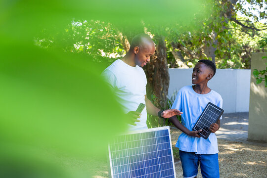African American father and child in tees holding large, small solar panels testing meter in yard