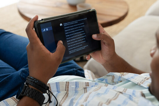 African American man reclining at home holding tablet in folio and reading for leisure