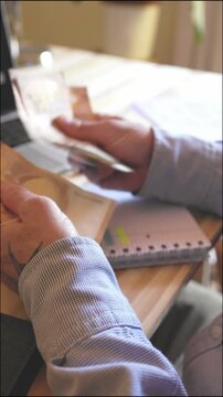 Close-up of male hands counting fifty euro banknotes over a wooden desk with a notebook and laptop in the background, representing home budgeting, financial planning, and income management