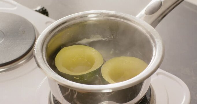 Electric burner is heating water in saucepan, two yellow halves are simmering to soften on cooktop
