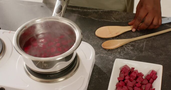 Man stirring pan with wooden spoon, placing spoon after mixing, burner heating, sauce bubbling