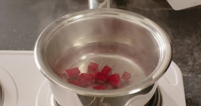 African American hand dropping red cubes into simmering saucepan on stove stirring color into water