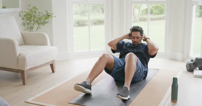 African-American man in shorts lying on back doing crunches, bicycle legs on mat home working core