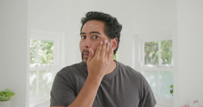 Mid-adult African man smoothing white cream after initial dollops, hydrating skin at home vanity