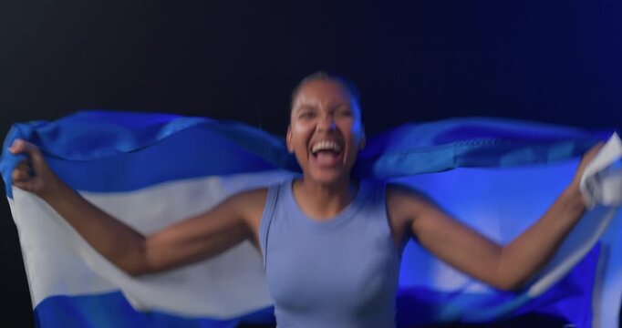 African American woman cheering as fan, waving blue-striped cloth in dark studio wearing tank top