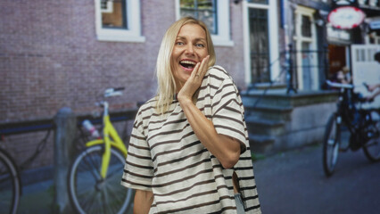 Fototapeta premium Woman with hand covering mouth showing surprised expression on a city street with bicycles and brick building; astonishment candid moment.