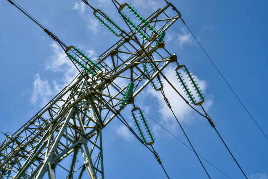 High-voltage transmission tower with power lines against a blue cloudy sky, Dutch electricity grid infrastructure for energy transition.